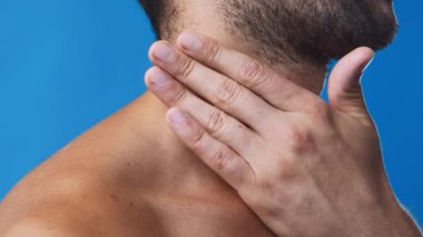 Bir adam, canlı, mavi bir arka plana karşı durduğunda boynuna hafifçe dokunur. Rahatlama ve kendine dikkat etme anını kucaklar ve kişisel refahına odaklanmayı önerir..