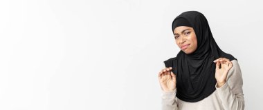 Disgusted black muslim woman in hijab feeling aversion about something, taking hands, posing over light background in studio, free space clipart