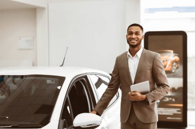 Otomobil satıcısı araba kapısı açıyor, otomobil galerisinde ayakta duran kameraya gülümseyen arabalar satıyor. Boşluğu Kopyala