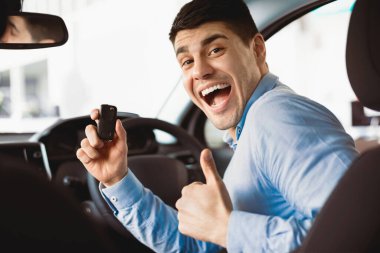 Yeni sahibi. Araba anahtarı elinde tutan ve galeride otururken el hareketi yapan heyecanlı adam.