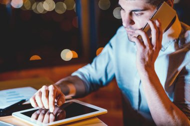 İş hayatı tarzı. Modern Ofiste Oturan Dijital Tablet Kullanarak Cep Telefonu Konuşan Ciddi İşadamı. Düşük Işık