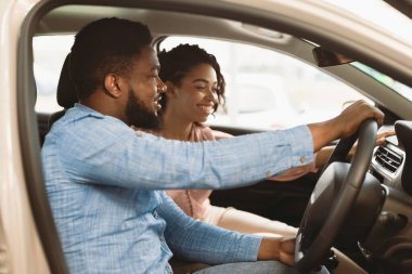 Test Drive. Happy Afro Spouses Sitting In Car Choosing Family Auto In Dealership Showroom. Selective Focus