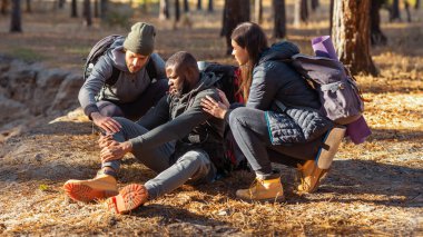 Arkadaşları yaralı bacağıyla zenci adama yardım ediyor, ormanda birlikte yürüyüş yapıyor.
