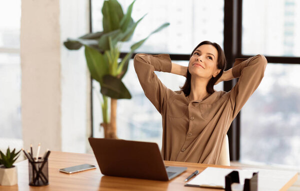 Time For Break. Successful young business woman stretching hands at workplace, looking up, free space