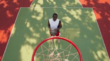 Afrikalı Amerikalı basketbolcu çemberin altında duruyor, güneş ışığıyla aydınlatılan açık hava sahasına atış yapmaya hazırlanıyor..