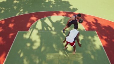 İki çok ırklı erkek açık hava sahasında bir basketbol maçında yeteneklerini ve çevikliklerini sergileyerek güneşli havalarda yarışıyorlar..