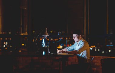 Bilgisayarda çalışan neşeli adam gece geç saatlere kadar modern ofiste internette geziniyor. Metin için Boşluk