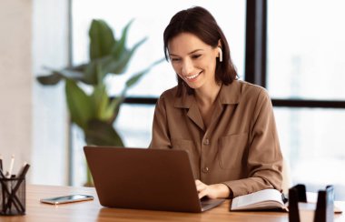 Mutlu İşçi. Kulaklıkla gülümseyen bir kızın portresi. Laptop kullanıyor, ofiste oturuyor ve müzik dinliyor.