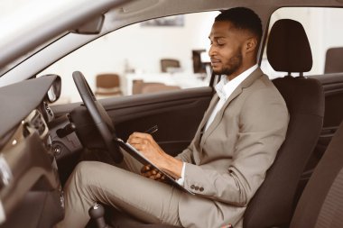 Otomobil satıcısı, galeride satmadan önce otomobili kontrol ederken not alıyor. Seçici Odaklanma