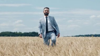 Buğday tarlasında, açık mavi gökyüzünün altında şık bir takım elbise giymiş, doğa ve entelektüelliğin bir karışımını sergileyen bir adam güvenle yürür..