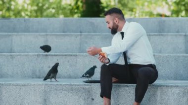 Resmi giyinmiş bir adam açık hava basamaklarında oturur, bir şeyler yer ve ona yaklaşan kuşları gözlemler..