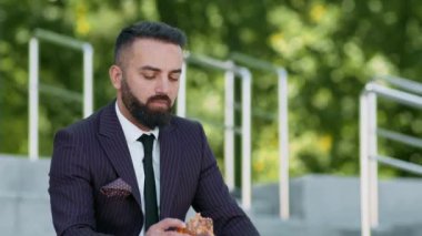 Çizgili takım elbiseli bir adam sıcak bir öğleden sonra dışarıda otururken kızarmış tavuktan bir ısırık alır..