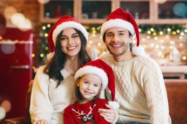 Sıcak, küçük bir aile Noel için hazırlanıyor, koltukta oturuyor, dekore edilmiş mutfağın üzerinde kameraya gülümsüyor, boş yer var.