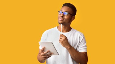 Düşünceli editör. Elinde not defteri ve kalemle turuncu duvarın üzerindeki boşluğa bakan hayalperest siyahi adamın portresi.