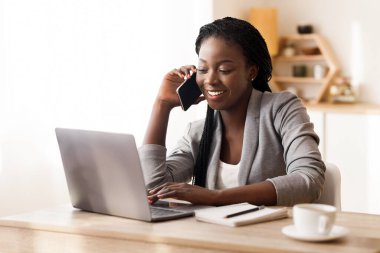 İş hayatı. Afrikalı iş kadını cep telefonuyla konuşuyor ve modern ofiste dizüstü bilgisayarla çalışıyor. Boşluğu kopyala
