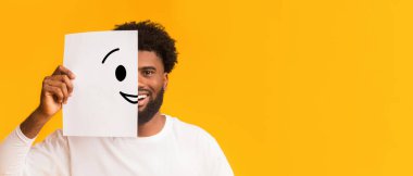 Gülen surat takınıyorum. Üzerinde gülen surat yazılı kağıt tutan siyah, neşeli adam, mutluluk ve neşe konsepti