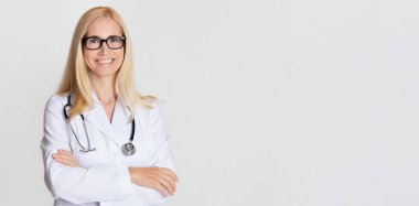 Steteskoplu kadın doktor gri arka planda poz veriyor. Kopya alanı olan panorama.