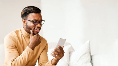 Modern İletişim. Evde koltukta oturan Afro Adam cep telefonu mesajları kullanıyormuş. Boşluğu Kopyala