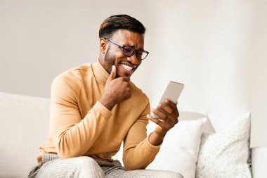 Neşeli Afro Adam cep telefonlu mesaj atıyor ya da internette komik haberler okuyor. Evdeki koltukta oturuyor. Boş Boşluk