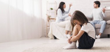 Aile çatışması. Küçük bir kız, anne babası evde kavga ettikten sonra ağlıyor, kafası aşağıda oturuyor, yüzünü dizlerine gizliyor, seçici bir şekilde odaklanıyor.