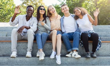 Mutlu arkadaşlar uluslararası öğrenciler yaz şehrinde birlikte vakit geçiriyorlar, merdivenlerde oturup gülümsüyorlar.