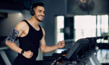 Spor salonunda koşu bandında koşan, koşan, spor yaparken müzik dinleyen, spor yapmaktan keyif alan, uzay kopyalayan, kablosuz kulaklıklı yakışıklı, kaslı Arap adam.