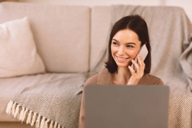 Aileyle konuşuyorum. Yerde oturup dizüstü bilgisayar kullanan, akıllı telefondan konuşan mutlu genç kadın.