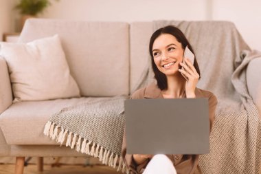 Hafta sonu Meselesi. Mutlu kız oturma odasında yerde oturuyor, dizüstü bilgisayar kullanıyor, akıllı telefonla konuşuyor, kopyalama uzayı...