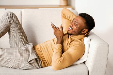 Neşeli Afrikalı Amerikalı Adam Akıllı Telefon Ses Asistanı ya da Evde Koltukta Dinlenen Hoparlör.