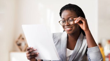 Evrak işi kavramı. Ofiste Mali Raporu okuyan mutlu Afrikalı iş kadını, sonuçtan memnun..