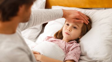 Adam hasta kızının ateşini ölçüyor, alnına dokunuyor, kapatıyor.