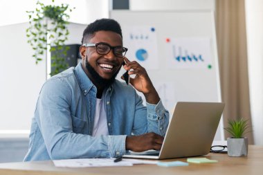 Ofiste dizüstü bilgisayarla çalışırken cep telefonuyla konuşan Mutlu Siyah Girişimciler.