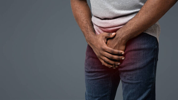 Cropped of black man holding his groin over white background, copy space
