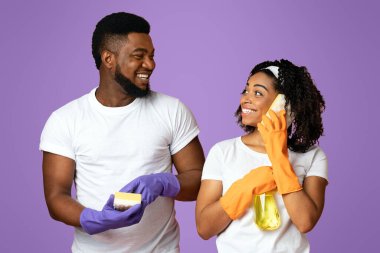 Çılgın Temizlik. Mutlu genç çift cep telefonu gibi sünger kullanıyor, evi düzenlerken birlikte eğleniyorlar, pembe arka plan ve boş alan.