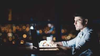 Modern Ofis 'te, Pencere kenarında oturan genç bir iş adamı dizüstü bilgisayarda fazla mesai yapıyor. Gece vardiyası. Boşluğu Kopyala, Panorama