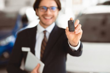 Yeni arabandan anahtar. Takım elbiseli mutlu satıcı, lüks bir mağazada otomatik kameranın anahtarlarını gösteriyor.