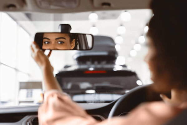 Новая машина. Африканская леди подстраивает зеркало, покупая VW, сидя в водительском кресле в салоне. Селективный фокус