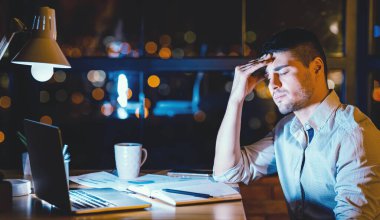 Baş ağrısı. Modern ofiste gece geç saatlere kadar çalışan yorgun menajer dizüstü bilgisayarda alnına dokunuyor. Boşluğu Kopyala