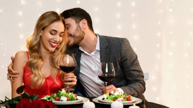 Loving Pair Dining In Restaurant, Having Romantic Date, Celebrating Valentines Day Together. Man Whispering Into Girlfriends Ear, Copy Space