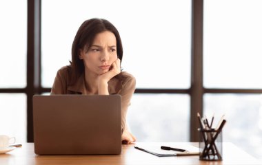 Can sıkıntısı. Modern ofisteki masada dizüstü bilgisayar kullanan üzgün genç kadın yöneticinin portresi.