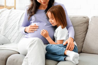 Meraklı küçük kız hamile annesinin karnını gözlemliyor. Evin içi, boş yer.