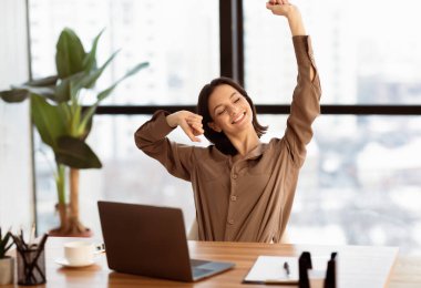 Mola zamanı. Başarılı genç bayan yönetici iş yerinde ellerini uzatıyor ve gülümsüyor.