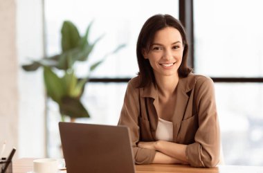 Mutlu ofis çalışanı. Kendine güvenen kadın yöneticinin portresi masada oturuyor, kollarını kavuşturuyor, kameraya bakıyor, telif boşluğuna bakıyor.