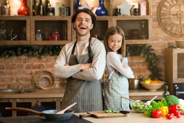 Önlüklü baba ve kızı mutfak arka planında kollarını kavuşturmuş poz veriyor, birlikte yemek pişiriyor, boş alan yaratıyor.