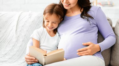 Anaokulundaki mutlu kız evde hamile annesiyle kitap okurken eğleniyor, kapat.