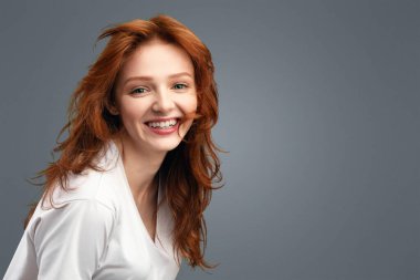 Beyaz arka planda kameraya gülümseyen, üzerinde tişört olan kızıl saçlı güzel bir bayan portresi. Stüdyoda neşeli gençlik pozu. Gençlik, Olumlu Duygular Konsepti