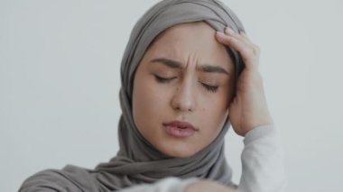 Gri tesettürlü bir kadın derin düşüncelere dalmış, ciddi bir ifadeyle hafifçe alnına dokunuyor..