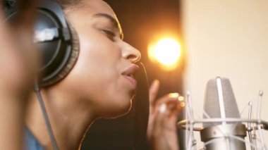 Sıcak ışıklarla aydınlatılmış samimi bir kayıt stüdyosunda şarkı söyleyen Afrikalı Amerikalı bir kadın duygularını ifade ediyor..