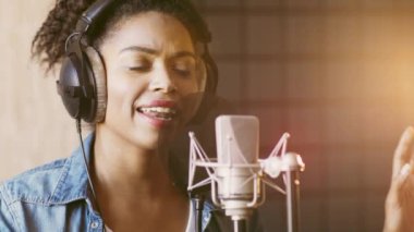 Afrikalı Amerikalı bir kadın bir müzik stüdyosunda kulaklık takarken mikrofona tutkuyla şarkı söylüyor..
