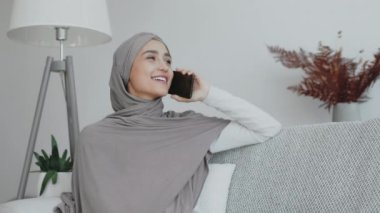 Gri tesettürlü bir kadın akıllı telefonuyla sohbet eder, rahat bir ortamda rahatlama yayar..